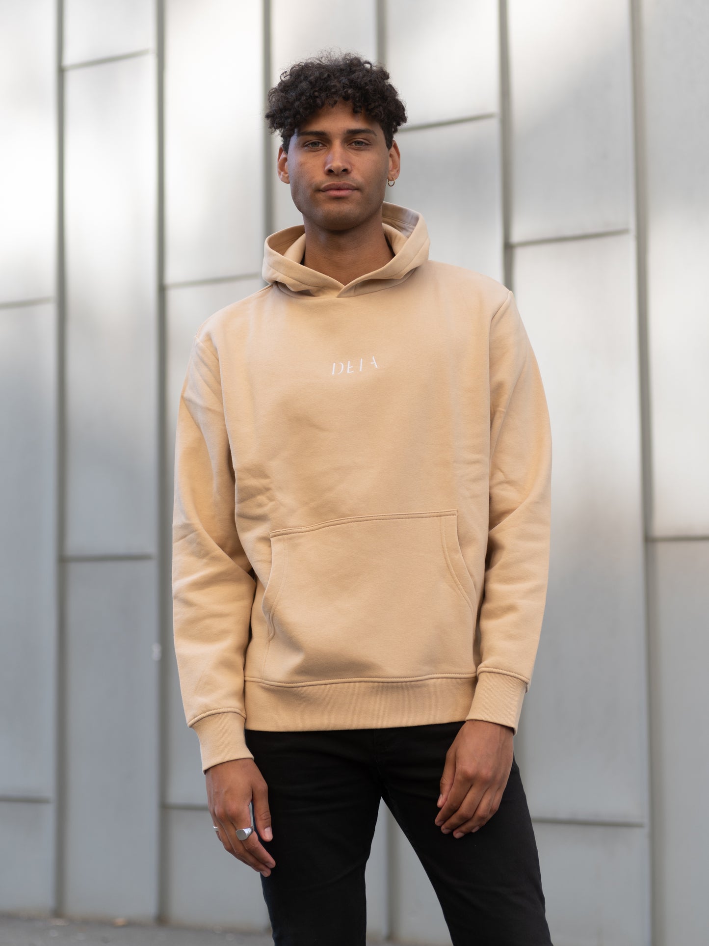 Herre med beige hoodie, med logo brodert på brystet 