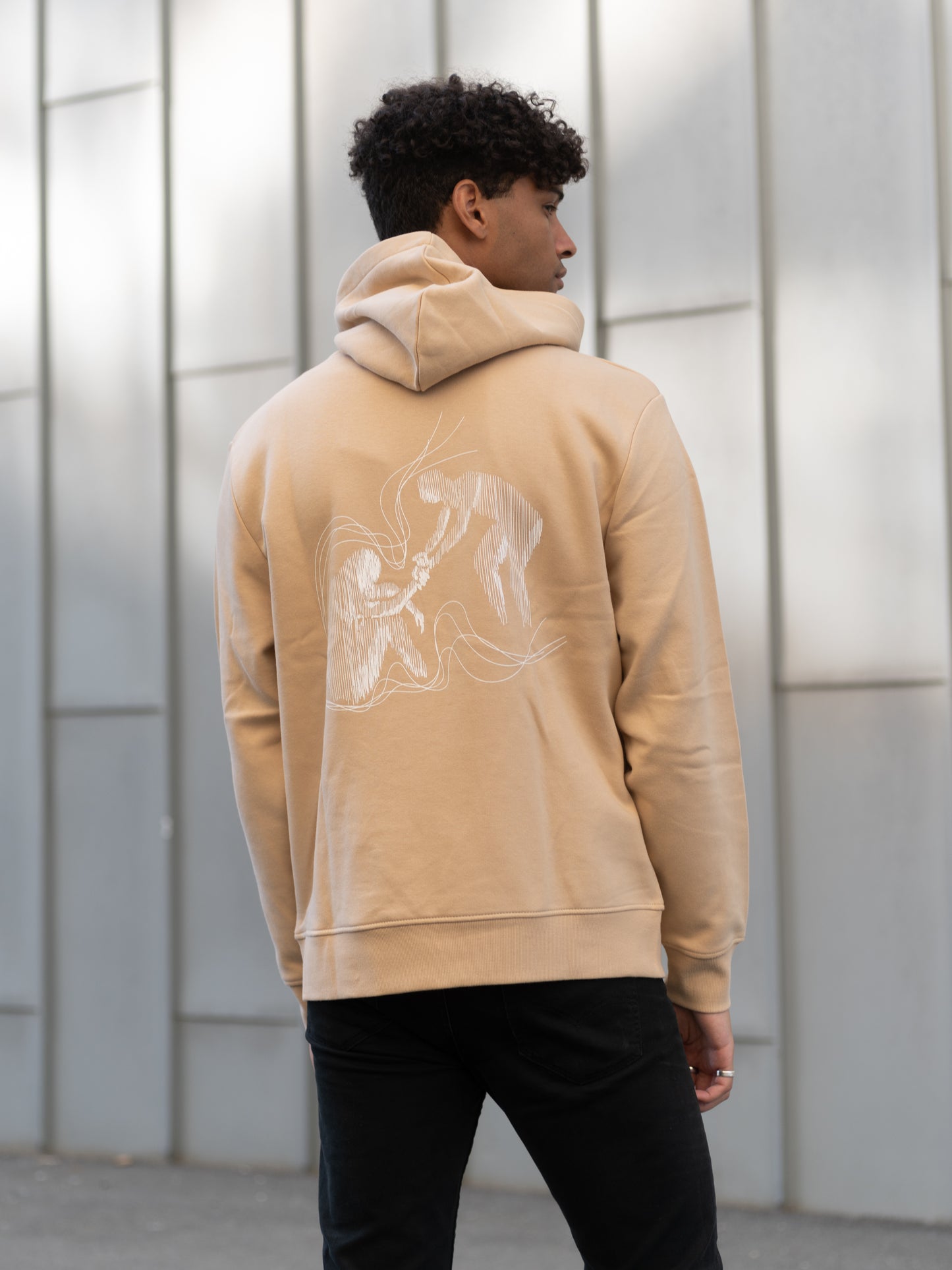 Herre med beige hoodie. Modellen viser ryggen, som inneholder en illustrasjon med et fokus på metal helse.